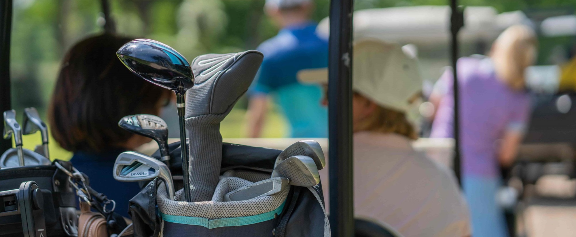 Golfclubs in een golftas met mensen op de achtergrond tijdens een zonnige dag op een van de golfbanen in Hart van Limburg.
