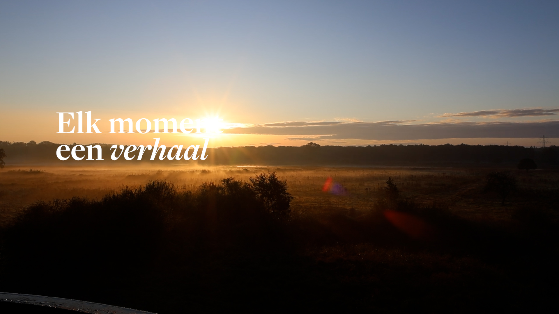 Zonsopkomst boven een nevelig landschap met de tekst ‘Elk moment een verhaal’ in beeld.