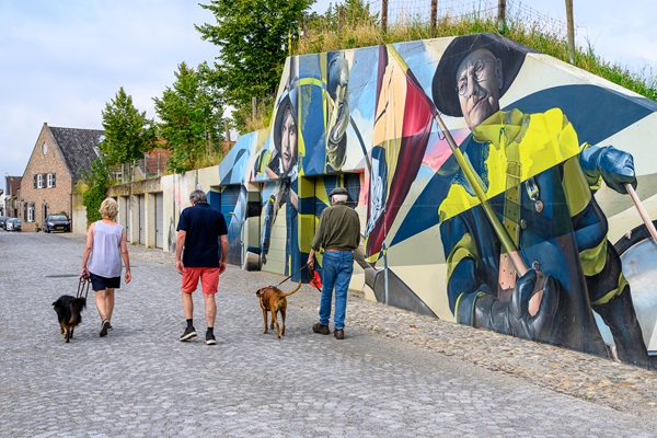 Hikers with dogs walk past Stevensweert street art depicting the Spanish conquerors