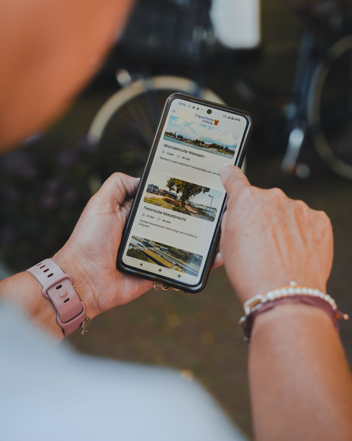 Eine Person hält ein Smartphone mit geöffneter Erfgoed Route Limburg App, mit der eine Route der Legende von Sankt Georg und dem Drachen entdeckt wird