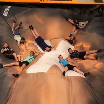 Groep kinderen ligt lachend op een grote opblaasbare trampoline tijdens een actief kinderfeestje in Limburg.