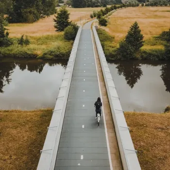 Fietser op een smal fietspad boven het water, omringd door groen en velden in Hart van Limburg.