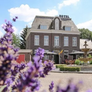 Het voormalige klooster Hotel-restaurant De Abdij met terras en fontein op de voorgrond, omringd door bloeiende planten.